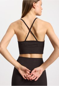 Reggiseno sportivo nero a coste con spalline incrociate. Presenta un design aderente e una costruzione senza cuciture. Tessuto strutturato e design minimalista.