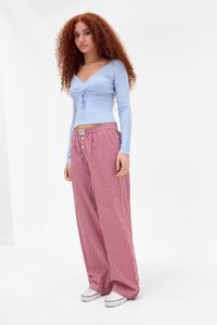 Top cu mâneci lungi, de culoare bleu deschis, cu detalii legate, asociat cu pantaloni largi în carouri roșii și albe. Adidașii albi completează ținuta.
