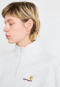 Lys grå fleece halv-zip genser med hevet krage og brodert Carhartt-logo i gul og burgunder på venstre bryst.