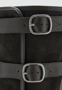 Bota de ante negra con dos correas de cuero que presentan hebillas de plata. Acabado texturizado con detalles de costura. Diseño a la mitad de la pantorrilla.