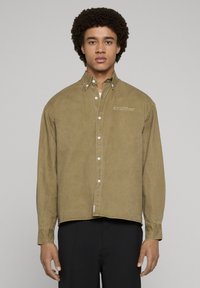 Verwaschenes olivgrünes Hemd zum Knöpfen mit lockerer Passform, ausgeprägtem Kragen und subtiler Stickerei auf der Brust. Baumwollmaterial.