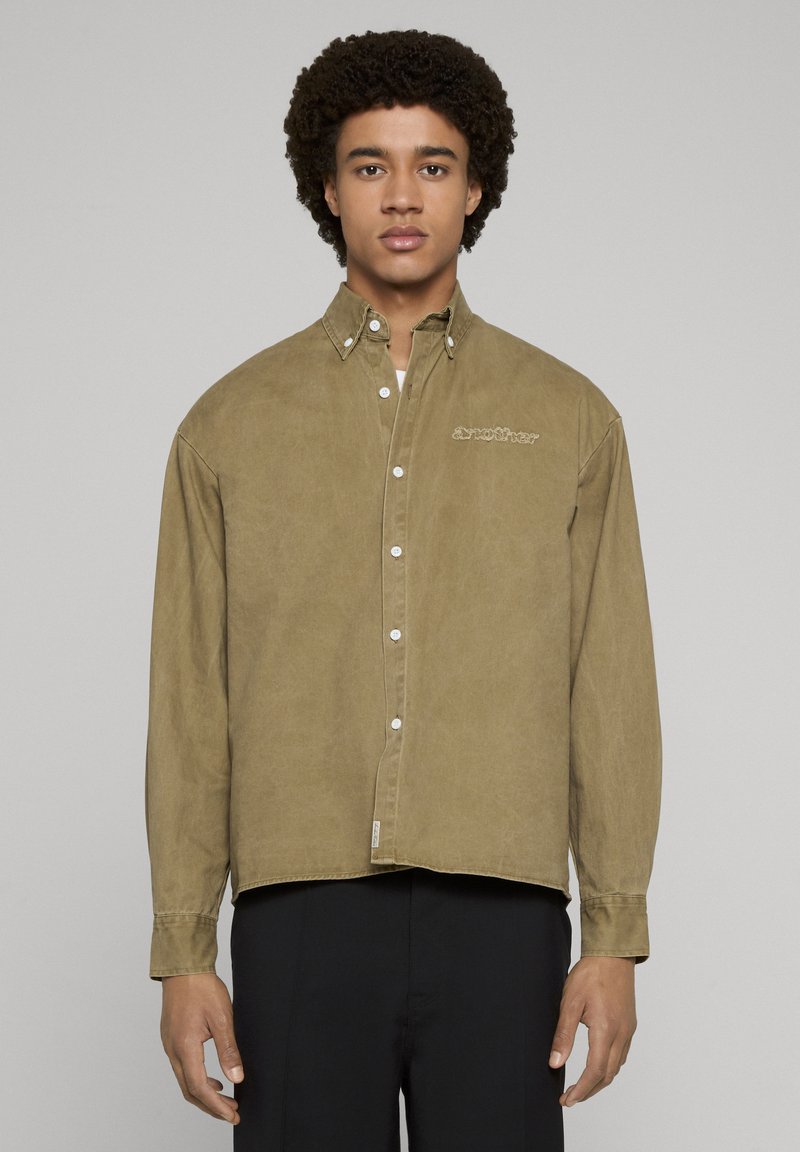 Verwaschenes olivgrünes Hemd zum Knöpfen mit lockerer Passform, ausgeprägtem Kragen und subtiler Stickerei auf der Brust. Baumwollmaterial.