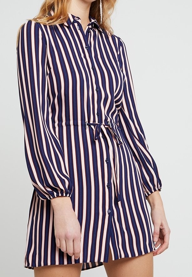 Pruhované košilové šaty s pruhy námořnické modré a růžové barvy, s knoflíky na předním díle, elastickým pasem a dlouhými nadýchanými rukávy. Hladká textura látky.