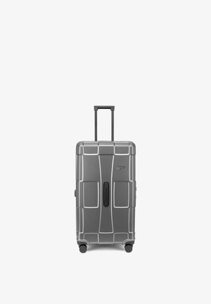 Valise rigide grise avec poignée rétractable, quatre roues pivotantes et poignée centrale, présentée en position verticale sur fond blanc.