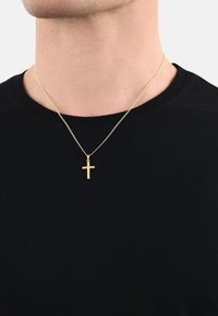 Collana con croce dorata su una fine catena, sospesa da una maglietta nera, caratterizzata da un design semplice e minimalista con una finitura lucida.