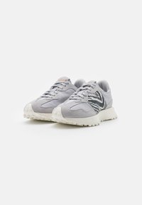 Zapatos deportivos grises que combinan ante y tejido, con acentos en negro en zigzag y una suela blanca texturizada.