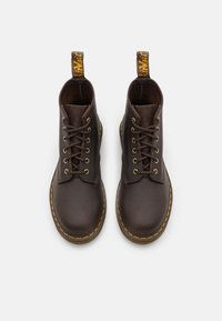 Bottines en cuir marron avec une texture lisse, bout rond, six œillets, lacets marron et semelle jaune surpiquée. Comprend une languette de tirage.