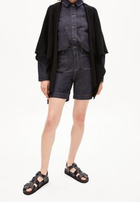 Jeansskjorta med beskuren design och knäppning, kombinerad med matchande högmidjade shorts. Svart stickad kofta och sandaler fulländar looken.