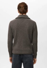 Suéter marrón de punto acanalado con cuello chal, que presenta una superficie texturizada y puños ajustados, combinado con jeans oscuros de mezclilla.