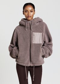 Giacca in pile di un morbido taupe con cappuccio, tasca con zip frontale, orlo regolabile e maniche raglan, caratterizzata da un aspetto testurizzato e accogliente.