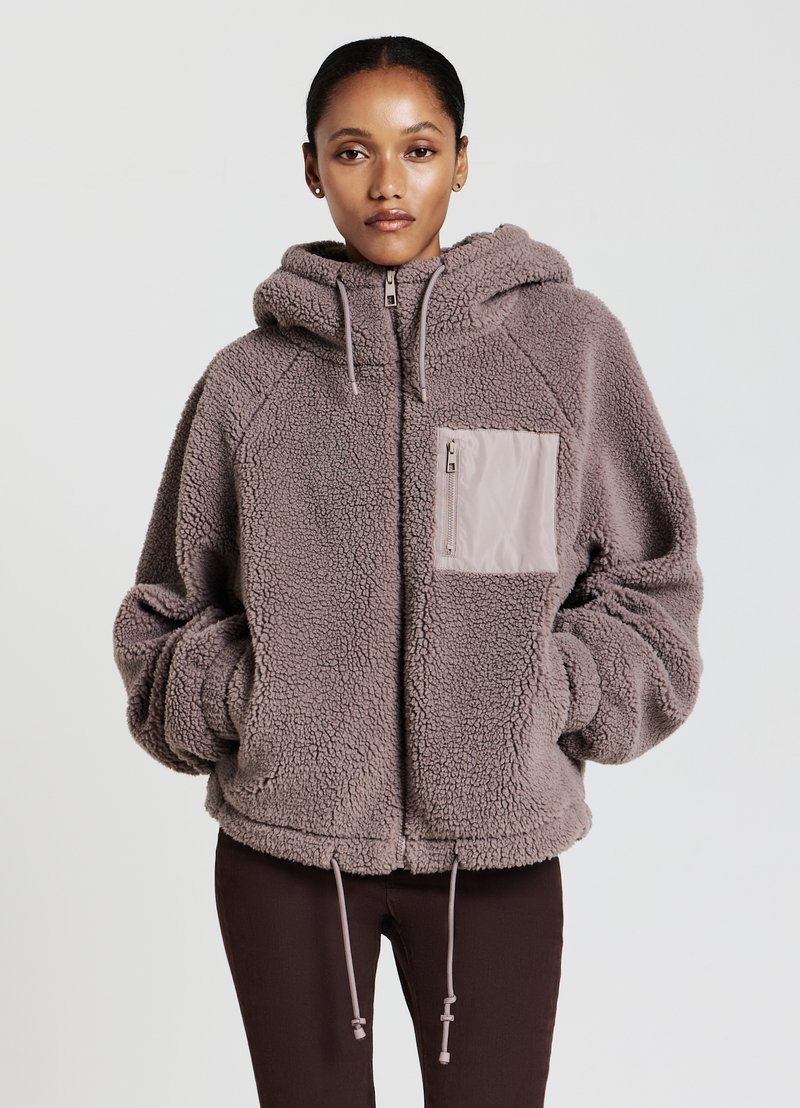 Giacca in pile di un morbido taupe con cappuccio, tasca con zip frontale, orlo regolabile e maniche raglan, caratterizzata da un aspetto testurizzato e accogliente.