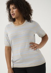 Pulover tricotat beige cu dungi bleu deschis, decolteu rotund, mâneci scurte și croială lejeră. Purtați-l cu pantaloni negri, modelul evidențiind designul.