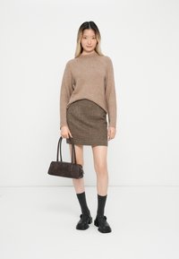 Brauner Strickpullover, Hahnentrittmuster-Rock, schwarze Schuhe, graue Socken. Dunkle Handtasche mit zwei Griffen. Einfaches, strukturiertes Design mit sanften Texturen.