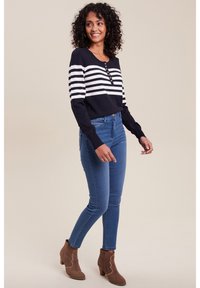 Langärmliges Oberteil mit navy- und weißen Streifen und Knopfdetails, kombiniert mit blauen Skinny Jeans und braunen Wildleder-Stiefeletten.