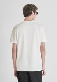 Camiseta de algodón blanca con mangas cortas, cuello redondo y corte relajado. Textura suave, diseño liso y sin gráficos ni patrones visibles.