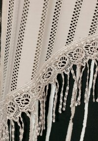 Gros plan d'une bordure en dentelle beige avec motif floral et fils pendants sur un tissu à rayures verticales noires et blanches.