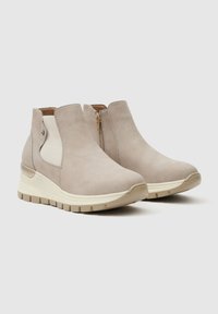 Botas de tobillo deslizables beige con paneles laterales elásticos blancos, cremalleras laterales, suelas gruesas de color blanco roto y un patrón de banda de rodadura texturizado.