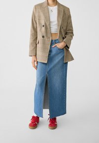 Blazer doppiopetto a quadri beige con accenti rossi, abbinato a una gonna di jeans con spacco alto e vivaci sneakers rosse.
