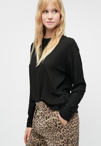 Sort langærmet top parret med beige leopardprint bukser. Toppen har en afslappet pasform, mens bukserne har en elastisk talje.