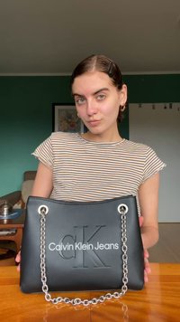 Svart fusk läder handväska med en kedjestropp, präglad "CK"-logotyp och "Calvin Klein Jeans" tryckt i vitt. Rektangulär form, slät textur.