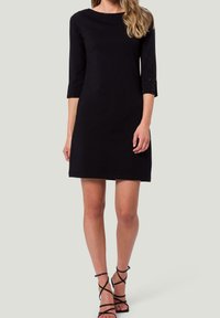 Robe noire avec des manches trois-quarts, présentant des accents texturés au niveau des poignets. Silhouette droite, ourlet au genou, faite d'un tissu doux.