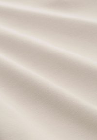 Miękka, kremowa tkanina o gładkiej fakturze, z delikatnymi fałdami i lekkim wyglądem, idealna do różnych zastosowań tekstylnych.