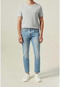 T-shirt gris à manches courtes, jean délavé clair et baskets blanches. Le t-shirt est ajusté, le jean légèrement fuselé avec une texture délavée.