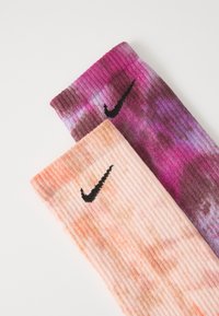 To par med Nike-sokker: en i nyanser av rosa og lilla, den andre i fersken og krem, begge med ribbestruktur og svart logo.