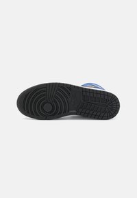 Svart gummisula på sneaker med ett mönster för texturerat grepp, cirkulär logotypdetalj och blå accenter längs kanten.