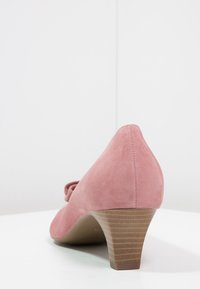 Scarpa con tacco alto in suede rosa, con retro curvo, dettaglio a fiocco davanti e tacco in legno impilato. Tessuto liscio con una finitura opaca.