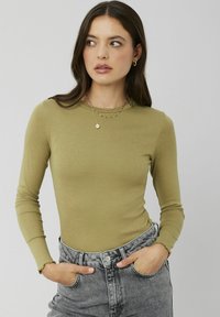 Haut à manches longues vert olive avec un design ajusté et une texture côtelée. Associé à un jean en denim gris taille haute, avec des poignets effilochés.