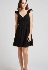 Robe noire sans manches avec des bretelles à volants, décolleté en V et corsage froncé. Jupe fluide en forme de A, faite d'un tissu texturé.