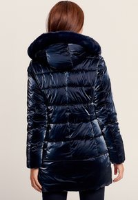 Marine blauwe gewatteerde pufferjas met een glanzende afwerking, voorzien van een met bont gevoerde capuchon en lange mouwen, ontworpen voor warmte en comfort.