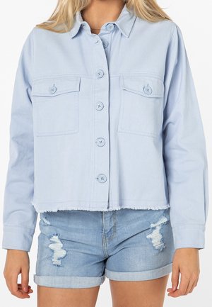Jasnoniebieska dżinsowa kurtka o kroju cropped, z dwiema przednimi kieszeniami, zapięciem na guziki i postrzępionym dołem, zestawiona z postrzępionymi szortami dżinsowymi.