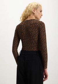 Top a maniche lunghe con un motivo leopardato marrone, realizzato in materiale elastico, abbinato a pantaloni neri a vita alta.