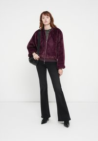 Bordo lažni krzneni bomber jakna s zatvaračem, uparena s crnim zvonastim hlačama i malom crnom torbicom za crossbody.