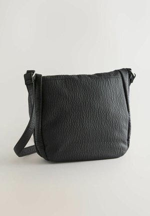 Zwarte leren crossbodytas met een gestructureerd oppervlak, verstelbare riem en een eenvoudig, gebogen ontwerp. Voorzien van een ritssluiting en zonder versieringen.