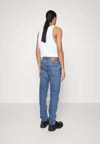 Blå denimjeans med rak passform, med en brun läderlapp på baksidan och en strukturerad yta, bärs med en vit linne.