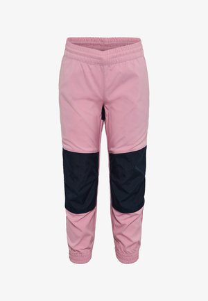 Lächelndes Kind mit langen blonden Haaren, das ein beigefarbenes T-Shirt mit Outdoor-Motiv, pink-schwarze Hosen und weiße Sneakers trägt und mit leicht ausgestreckten Armen steht.