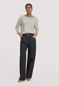 Helle graue Langarmbluse kombiniert mit hoch taillierten, weit geschnittenen, dunkelblauen Jeans. Die Jeans haben frontale Taschen und einen Knopfverschluss.