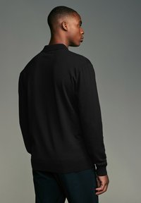 Melna adīta džemperis ar garām piedurknēm, ribotām aprocēm un apakšmalu, ar klasisku apkakli. Gluda tekstūra un pieguļošs dizains.