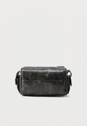 Trousse de toilette rectangulaire en cuir noir avec des poches latérales et une fermeture éclair sur le dessus, sur un fond clair uni.