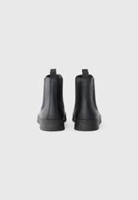 Botas negras de tobillo con parte superior de piel suave, suela de goma plana y lengüetas en la parte posterior; diseño simple y elegante con detalles de costura mínimos.