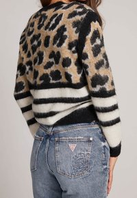 Pull en tricot imprimé léopard en marron, noir et crème avec des rayures horizontales noires et crème à l'ourlet, associé à un jean bleu délavé.