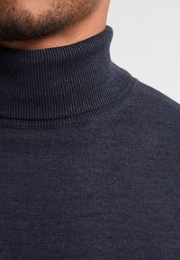 Maglione a collo alto di un blu navy scuro realizzato in tessuto a costine. Texture liscia con un design aderente, che mette in risalto il colletto e il materiale morbido.