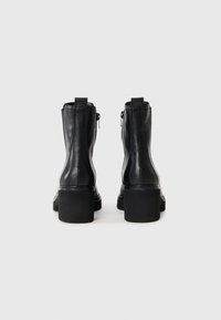 Bottes de cheville en cuir noir avec une texture lisse, fermeture éclair à l'arrière et un design de talon épais. Présente des coutures renforcées et des tirettes.