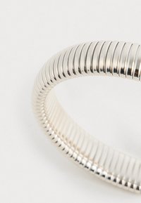Strieborný náramok v podobe špirály s textúrovaným, rýhovaným dizajnom, hladkým povrchom a kruhovým tvarom. Povrch odráža svetlo, čo zdôrazňuje jeho elegantný vzhľad.
