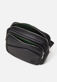 Borsa a tracolla nera in pelle con molteplici scomparti con zip, fodera verde e una superficie texturizzata. Accenti in metallo argentato.