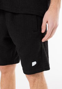 Pantaloni corti neri a coste realizzati in tessuto testurizzato, con tasche laterali e un piccolo logo bianco sul fondo della gamba.
