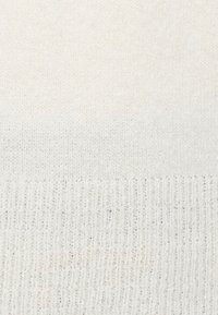 Gros plan d'un tissu tricoté blanc montrant des textures de tricot fines et côtelées.